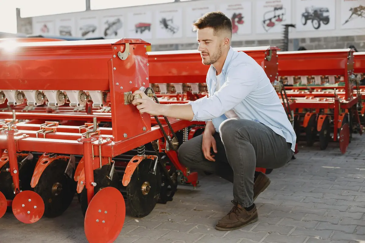 A man kneels beside a red aeration implement on display in an outdoor showroom.