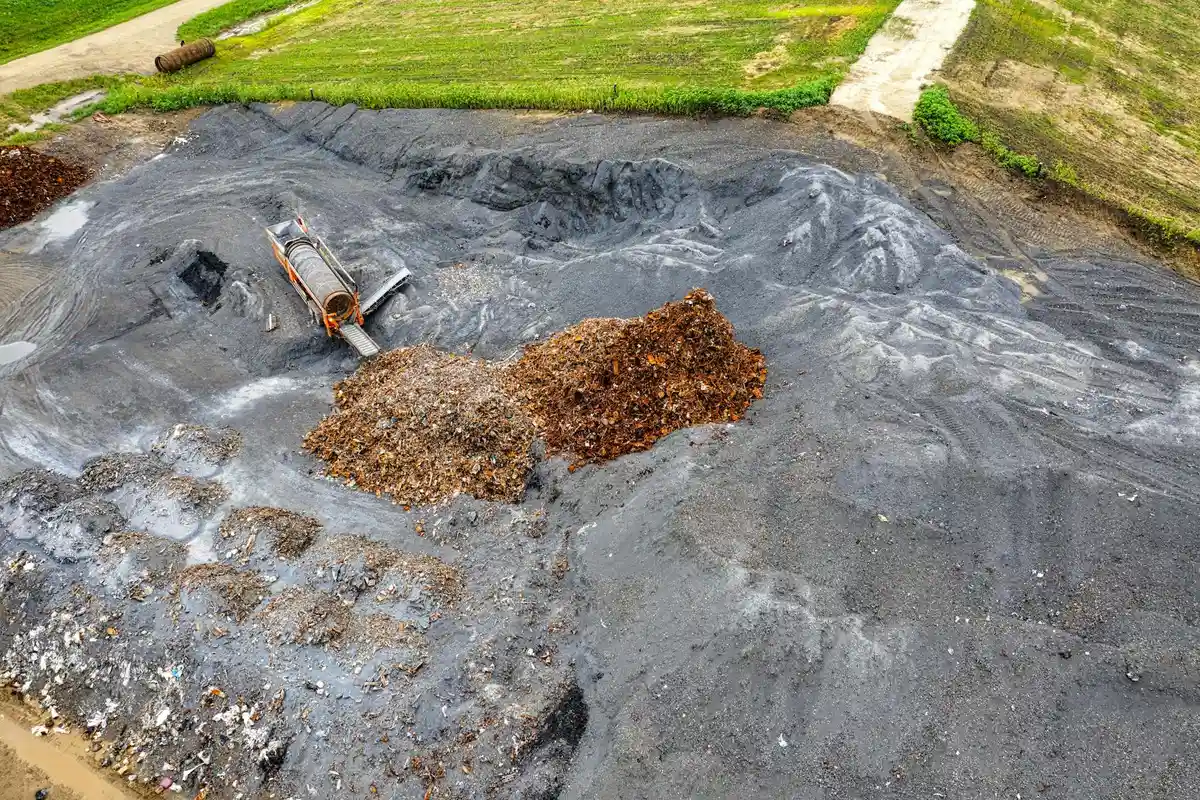 Exposed manure pile on a tarp with a small skid steer bucket nearby, illustrating poor storage for manure used as fertilizer.