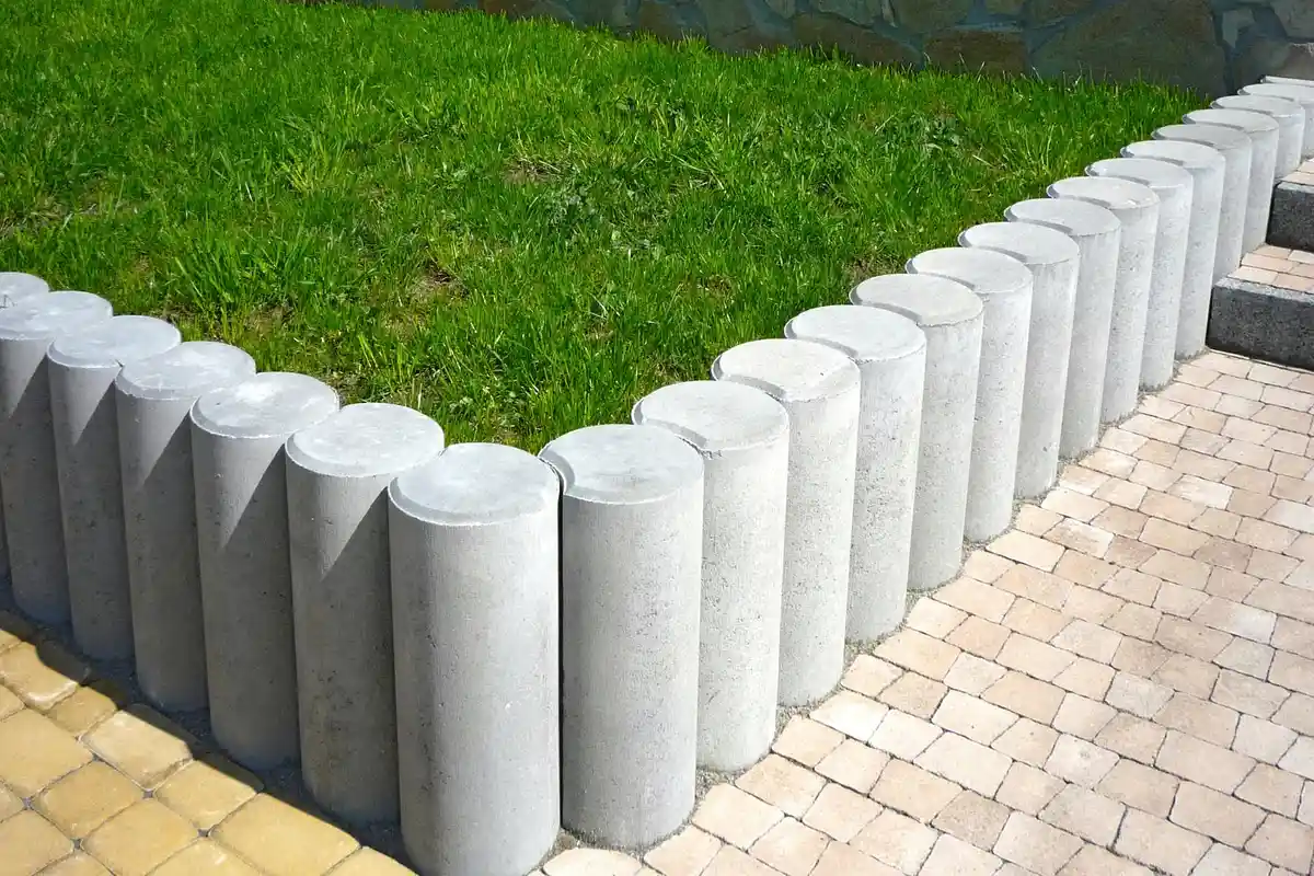 Row of cylindrical concrete lawn edging blocks forming a neat border between a green lawn and a paved walkway