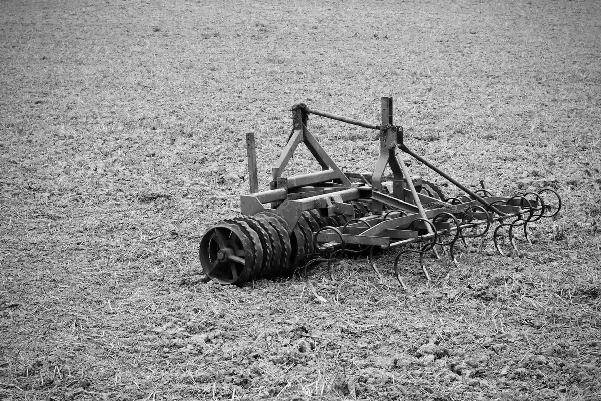 A core aeration machine with multiple tines rests on a dry, bare lawn, ready to perforate soil.