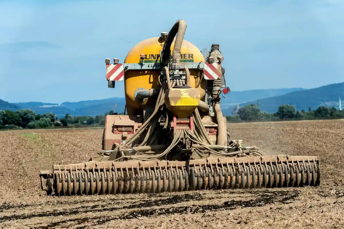 Yellow broadcast fertilizer spreader in a tilled field under a blue sky, ready to apply fertilizer.