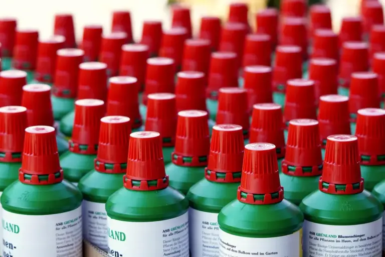 Rows of green fertilizer bottles with red caps lined up on a surface