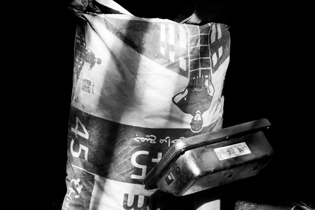 Black-and-white photo of a fertilizer bag and a small container on a dark surface, illustrating improper storage conditions.