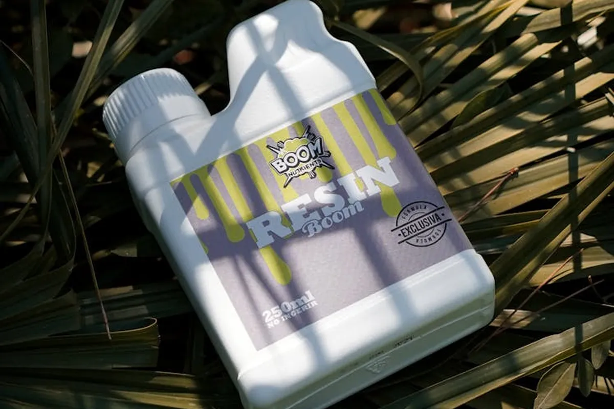 White plastic fertilizer bottle with a yellow and purple label resting on green plant leaves