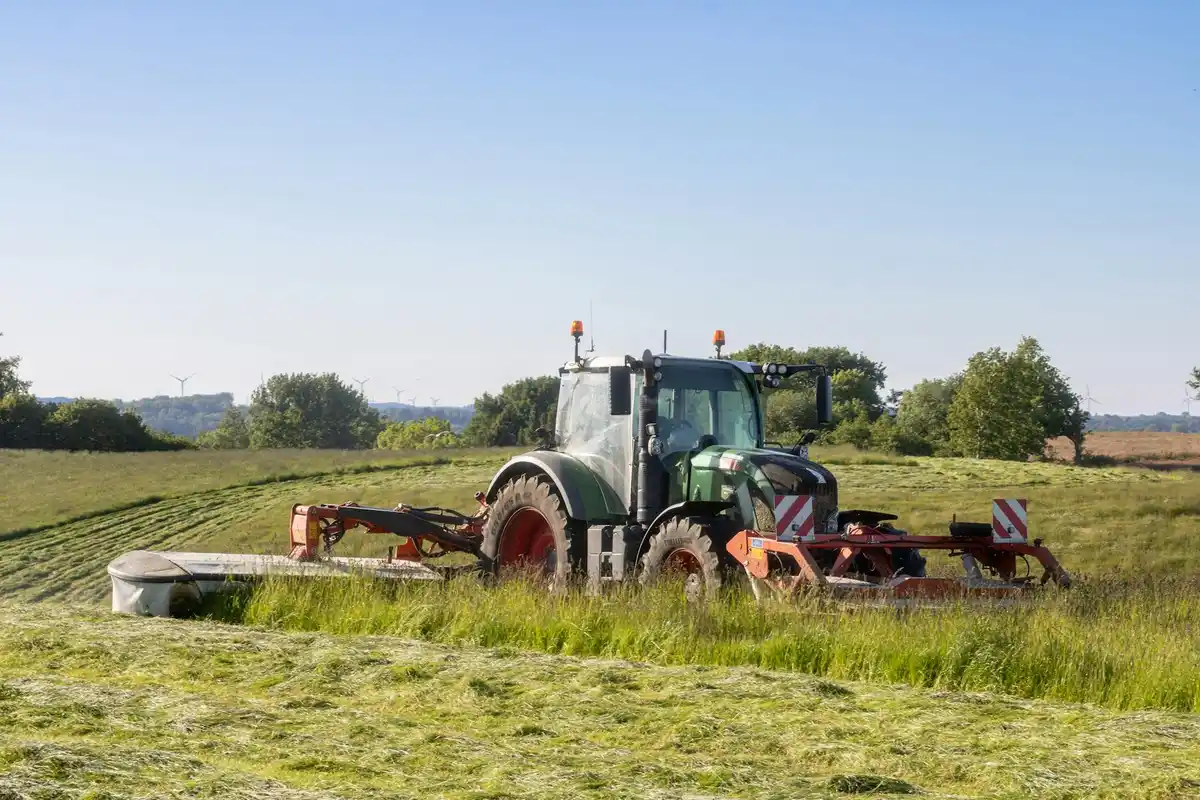 Green tractor mower with a cutting attachment in a sunny field.