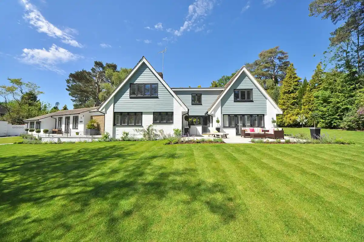 A wide, neatly mowed lawn in front of a modern two-story house with trees in the background.
