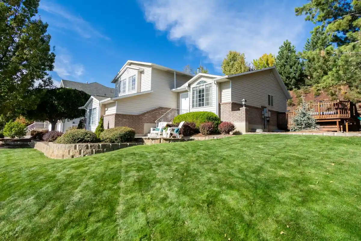 Front yard of a suburban house with a lush green lawn, stone edging, and a small patio with seating.