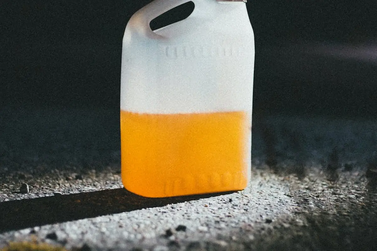 White plastic gasoline can with orange gasoline on a dark asphalt surface.