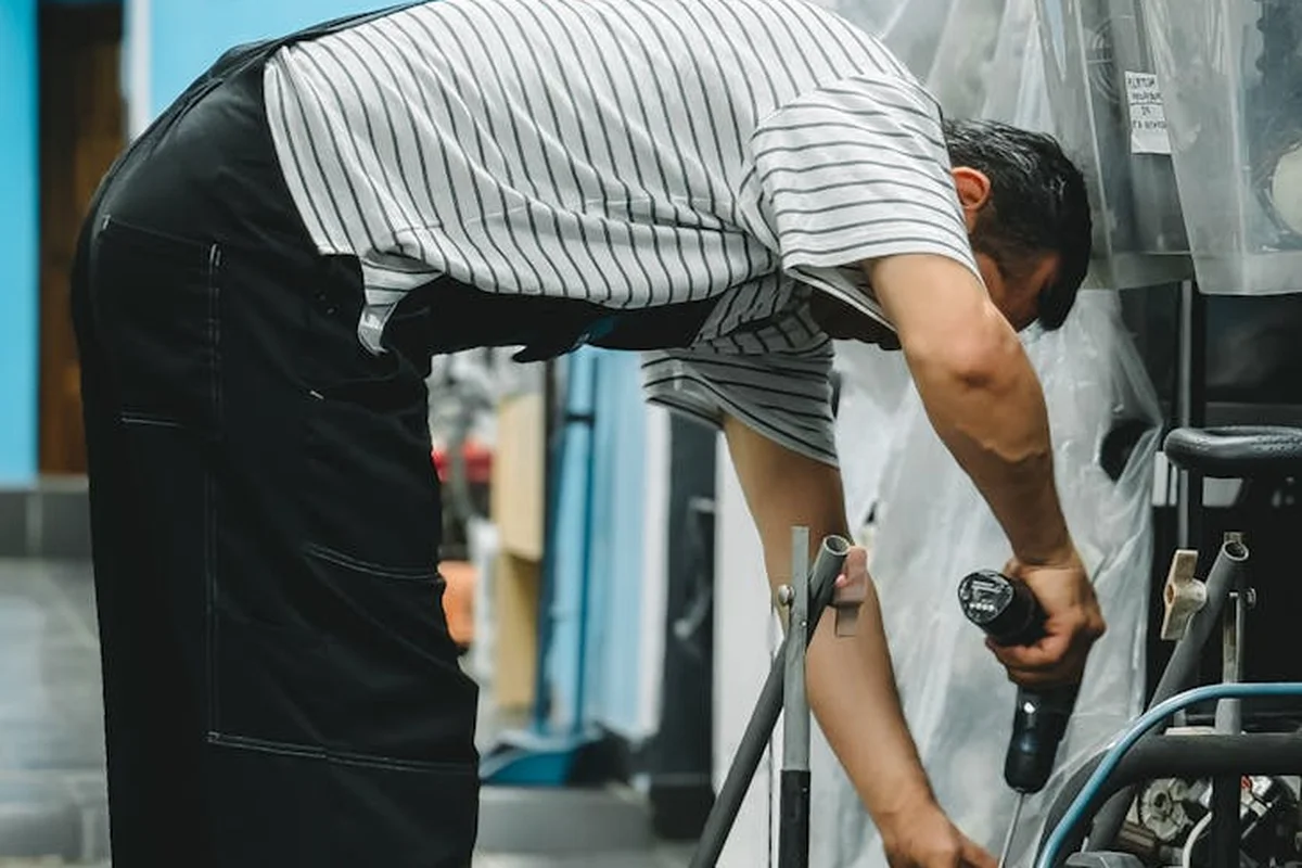 Person bending over to service a lawn mower in a workshop.