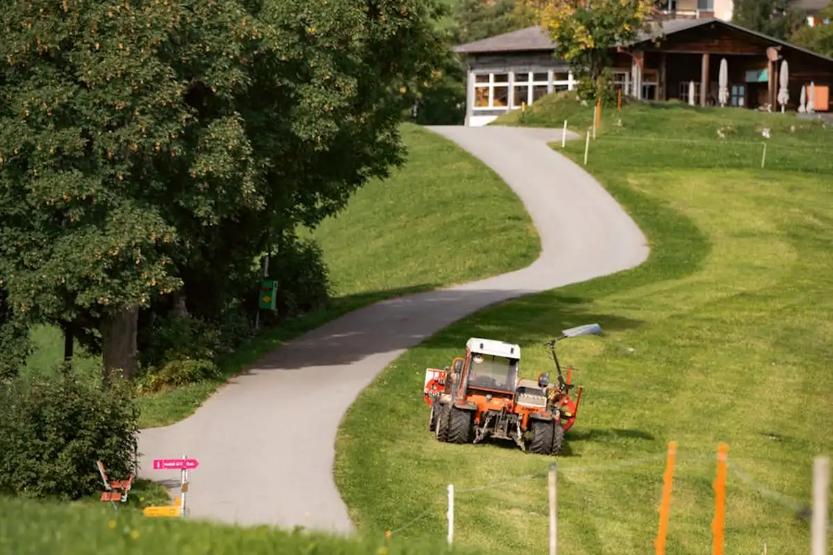 A lawn mower on a curved path in a grassy yard with a house in the background.