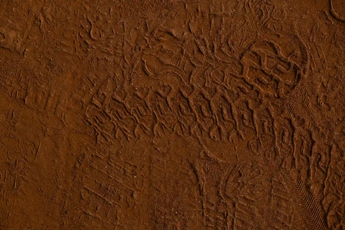 Close-up of red-brown heavy clay soil with footprints and tread marks illustrating surface compaction.