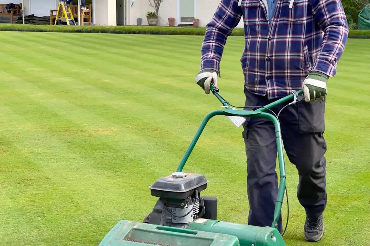 Person in plaid shirt operating a lawn aerator on a well-maintained green lawn