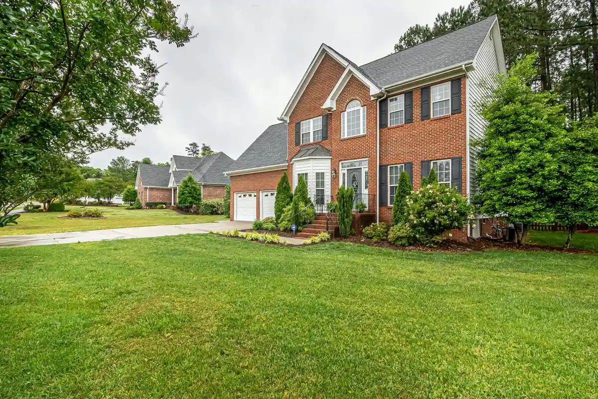 Front yard with a lush green lawn and a brick two-story house in a suburban neighborhood