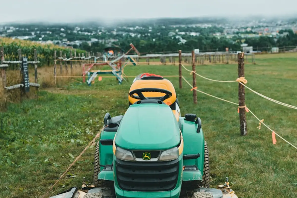 Green lawn tractor with an aeration attachment on a grassy field, fence posts and rural landscape in the background.