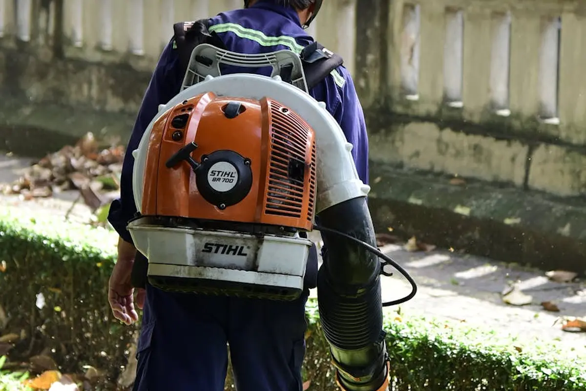 Lawn care professional wearing an orange Stihl backpack leaf blower on a residential property.