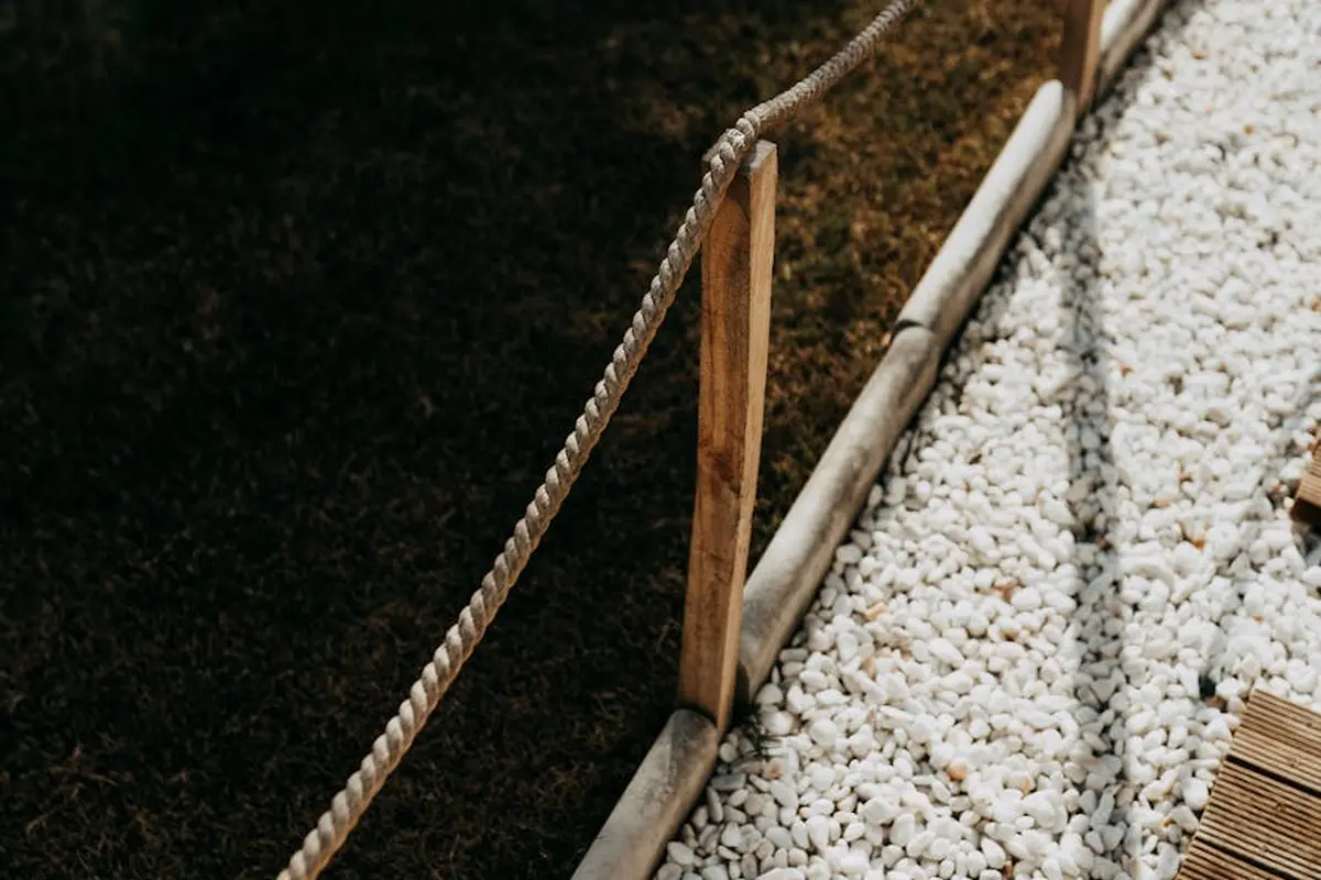 Close-up of a rope edging setup with a wooden stake along a border between dark soil and white gravel, illustrating a temporary edging method.