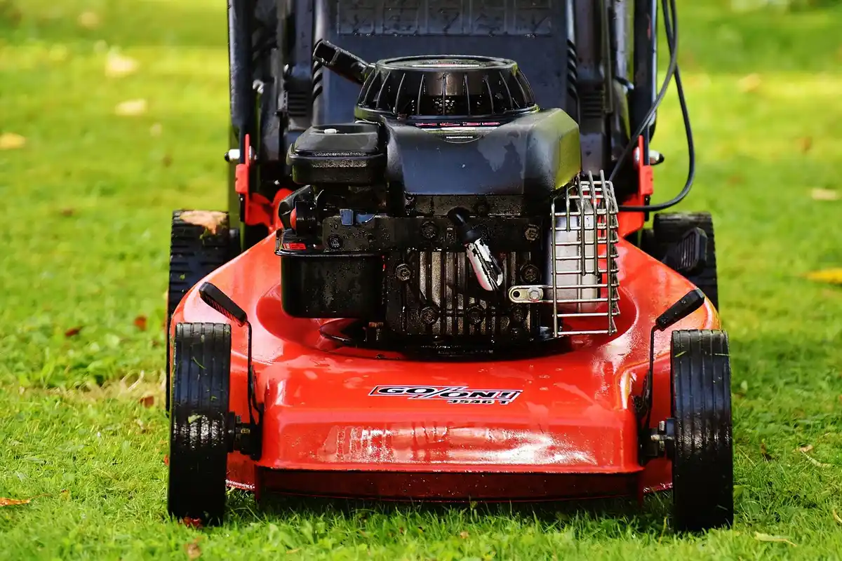 Red lawn mower with its blade area exposed on green grass.