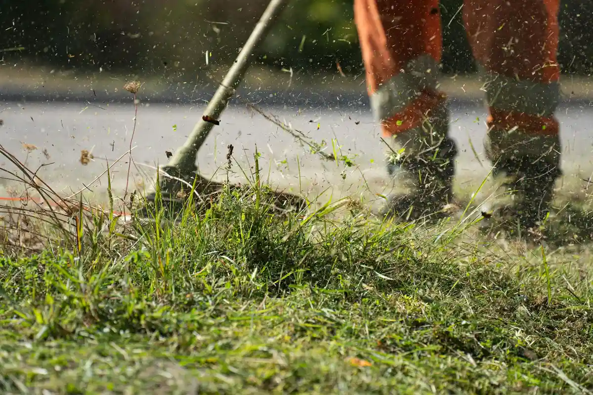 Lawn mowing scene with grass clippings in the air and a person wearing boots standing nearby