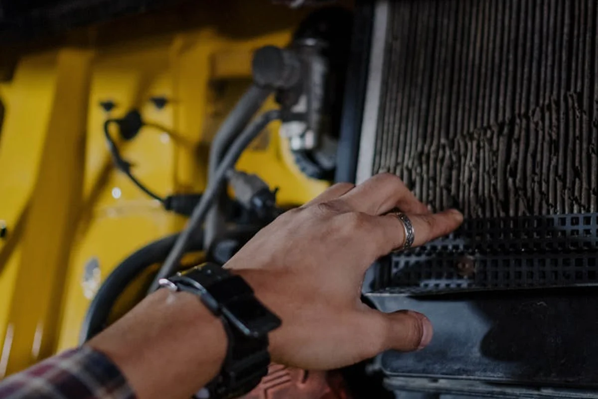 Close-up of a hand reaching into a lawn mower's filter housing area to inspect or clean the air and fuel filters.