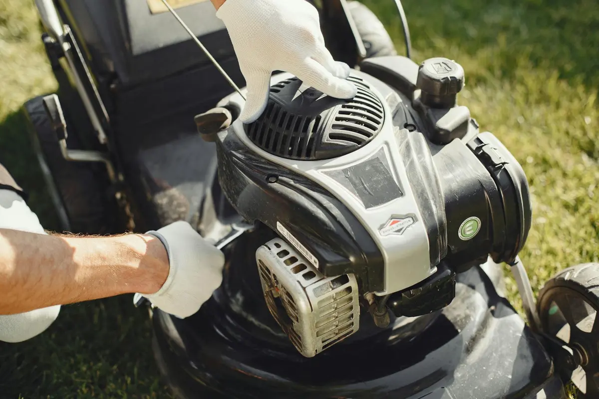 Person wearing gloves performing an oil change on a gas-powered lawn mower engine.