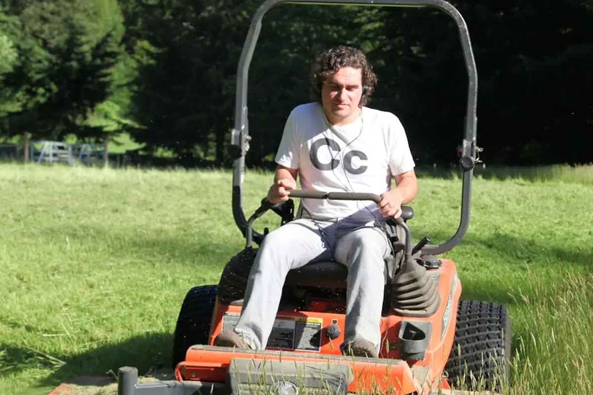 Person riding a lawn mower in a sunlit grassy field