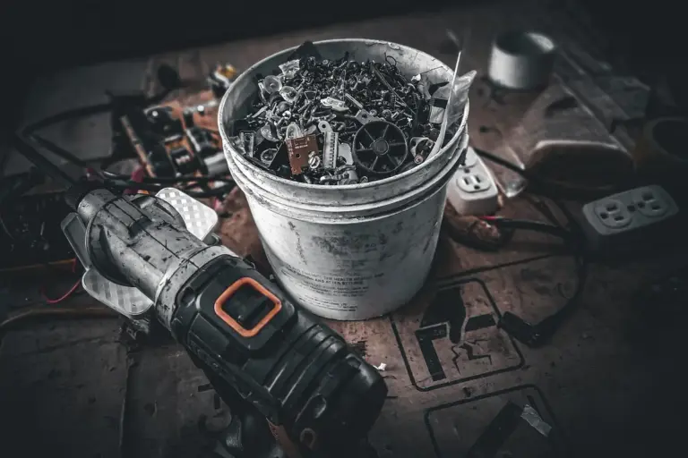 Cluttered workshop surface with a bucket filled with metal shavings and a power drill, illustrating lawn mower maintenance.