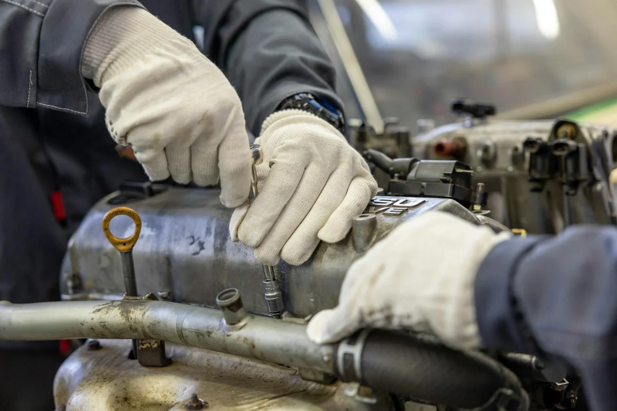Close-up of a technician wearing gloves inspecting a lawn mower engine to locate and diagnose the spark plug