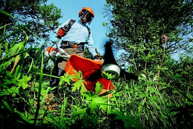 Person wearing safety helmet and gloves operating a gas-powered lawn mower in tall green grass