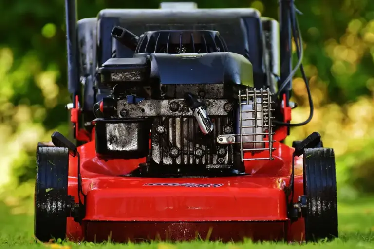 Front-facing red lawn mower on a green lawn with sunlight in the background.