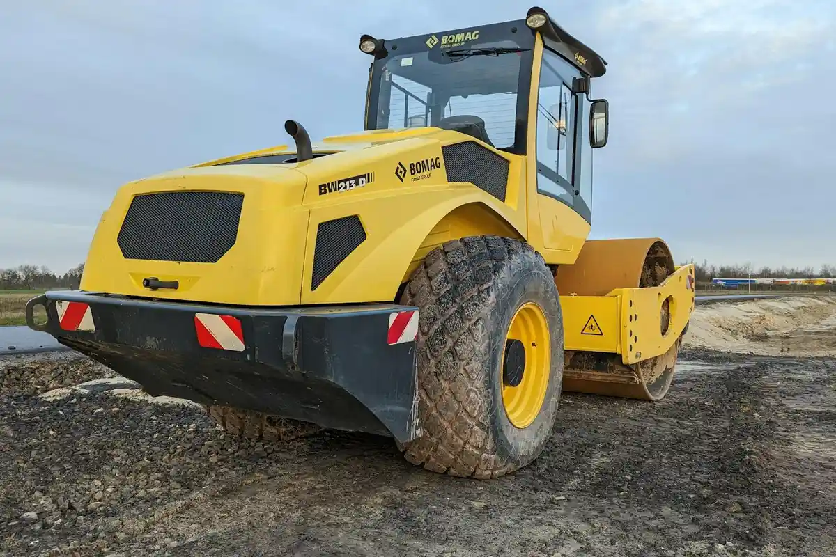 Yellow ride-on soil compactor/roller parked on dirt at an open site.