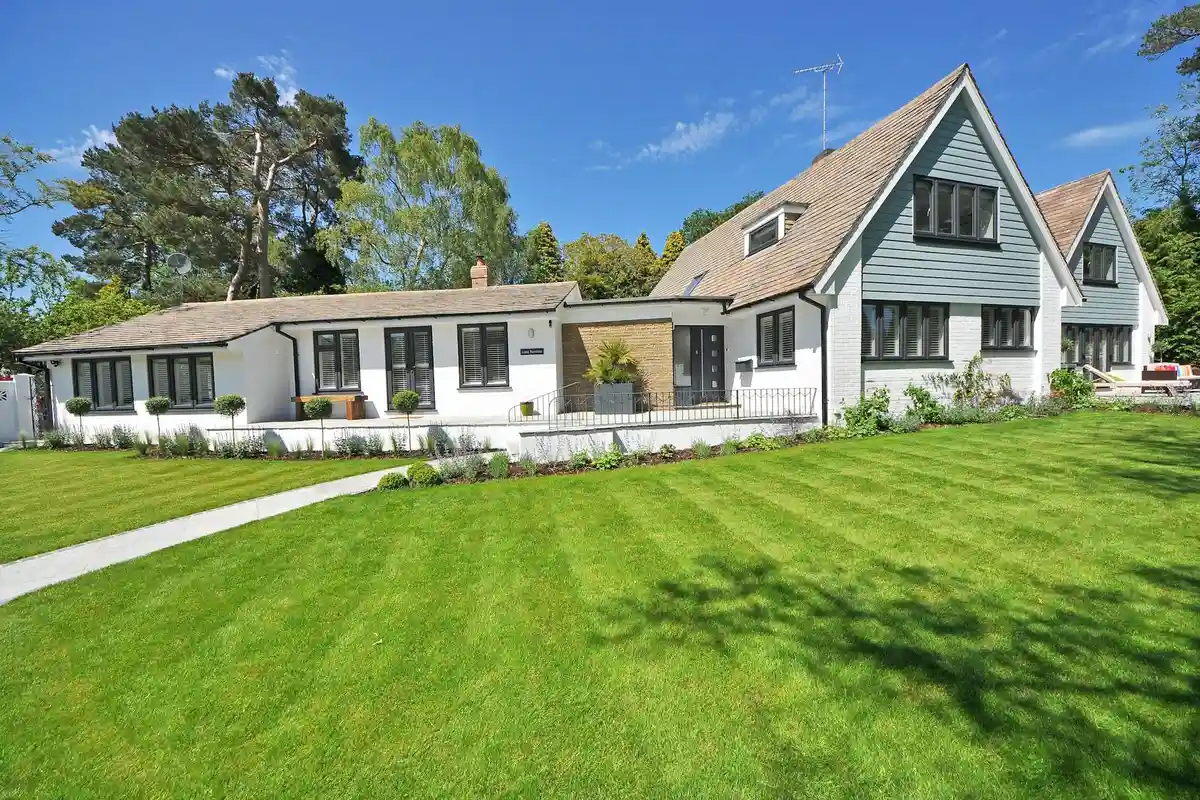 A large green lawn in front of a white suburban house with a clear blue sky.