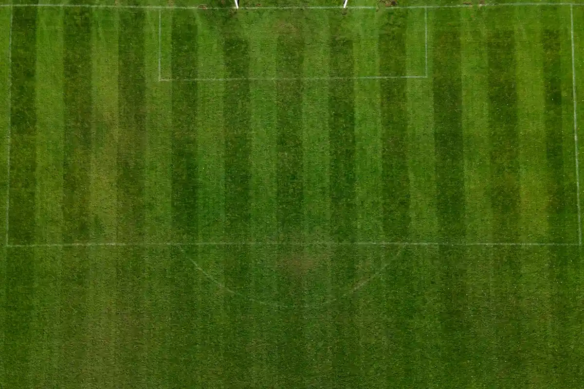 Aerial view of a sports field with alternating light and dark green mowing stripes across the grass.