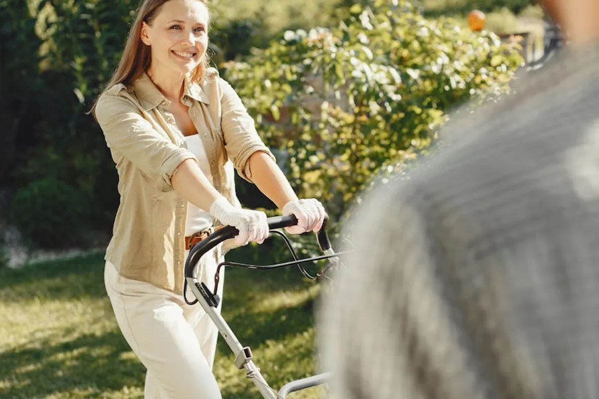Smiling woman pushing a lawn mower across a sunlit garden, illustrating mowing patterns