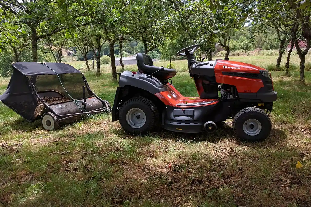 Red lawn tractor with a bagger attachment in a grassy yard with trees