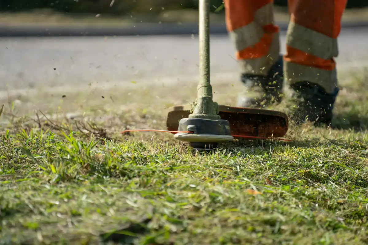 Close-up of a worker in orange safety gear operating a lawn aerator on a patch of grass