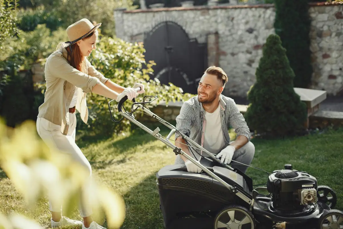 Two people operate a gas-powered lawn aerator in a sunny backyard.