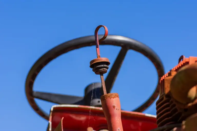 Close-up of a red lawn tractor battery terminal with a looped connector against a blue sky