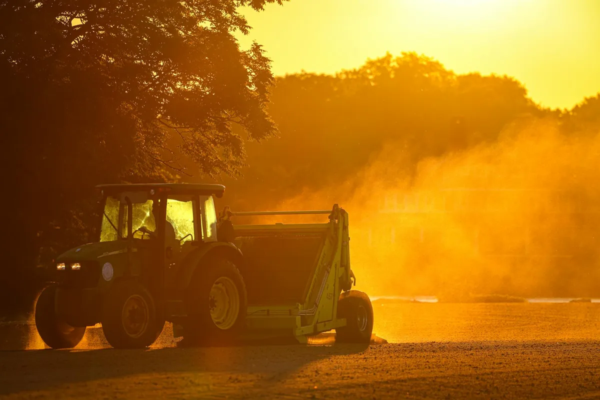 Sunlit lawn tractor at dusk with a plume of dust and smoke in the air, suggesting maintenance work.