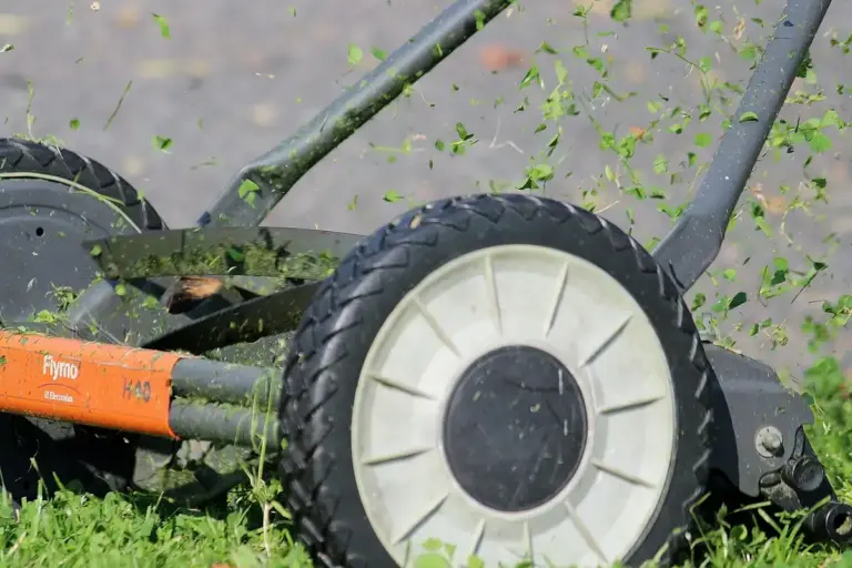 Close-up action shot of a lawn mower cutting grass with green clippings flying.