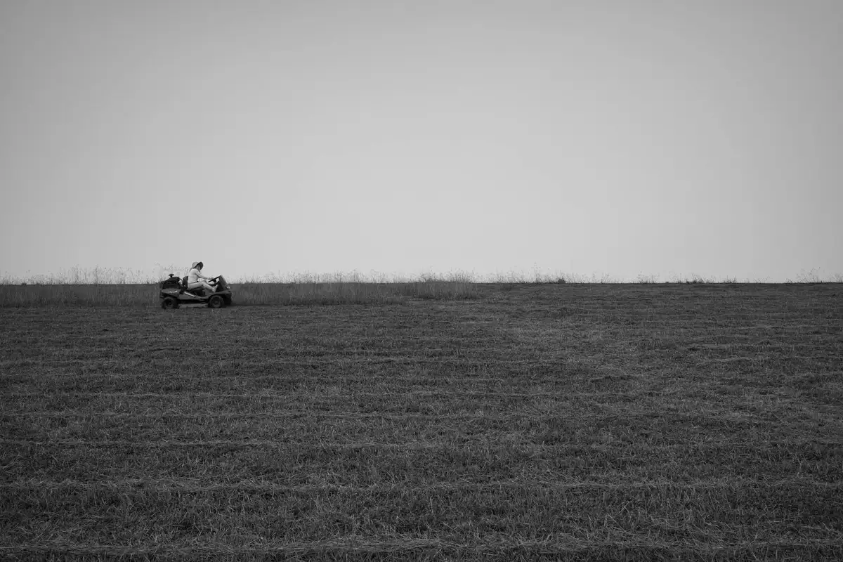 Black-and-white image of a small lawn mower on a vast open field, emphasizing space and safety for blade maintenance.