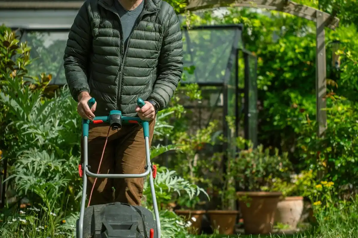 Person in a green jacket using a lawn mower in a lush garden