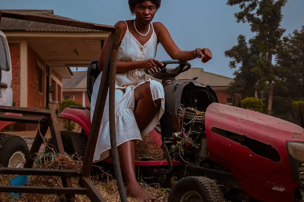 A person sits on a red lawn mower in a yard, preparing to operate it.