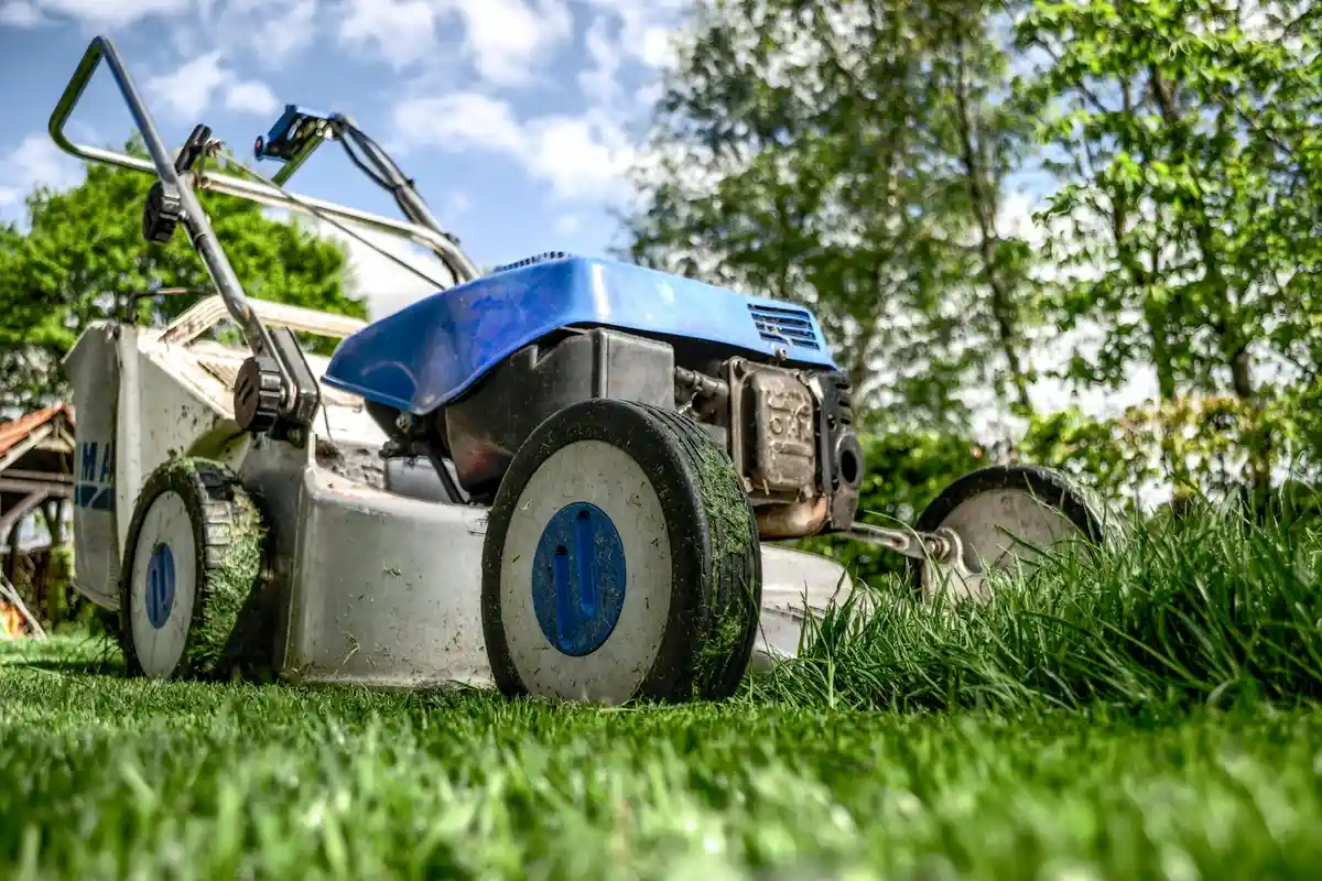 A mower resting on a well-maintained green lawn with trees in the background.