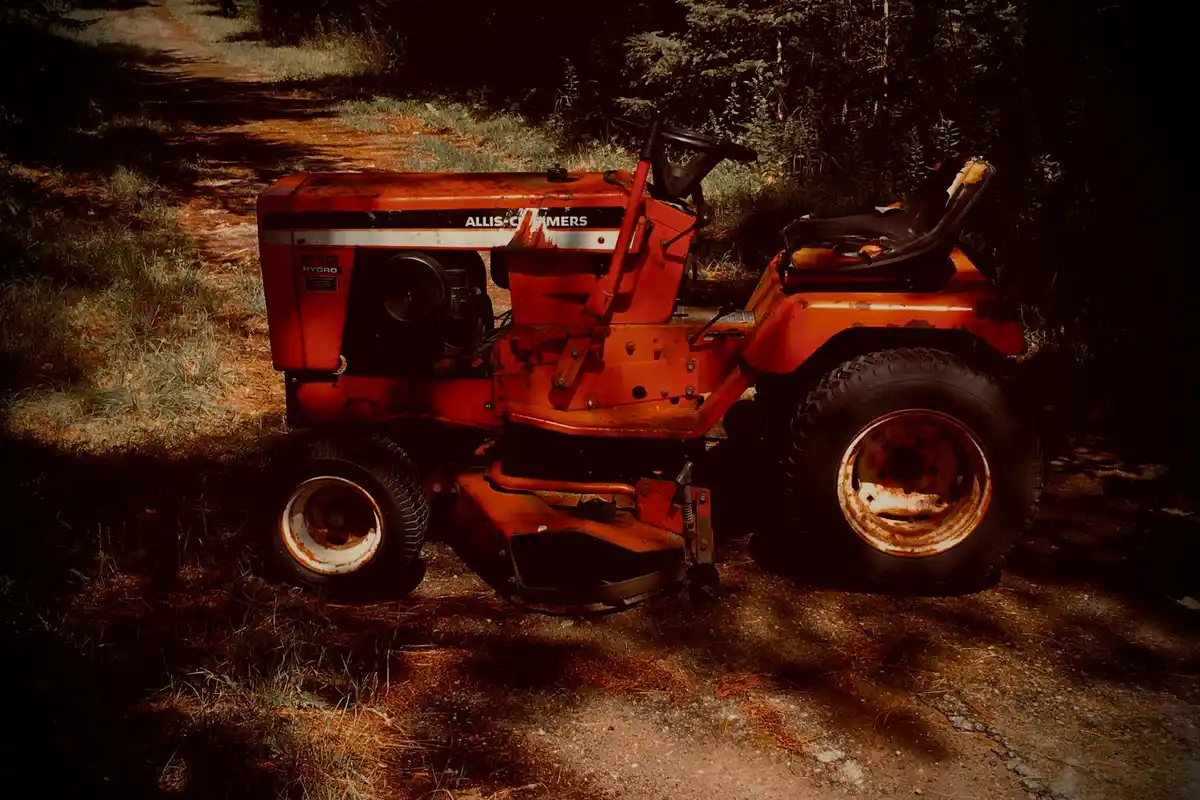 Red riding lawn mower parked outdoors on a dirt path, partially shaded.