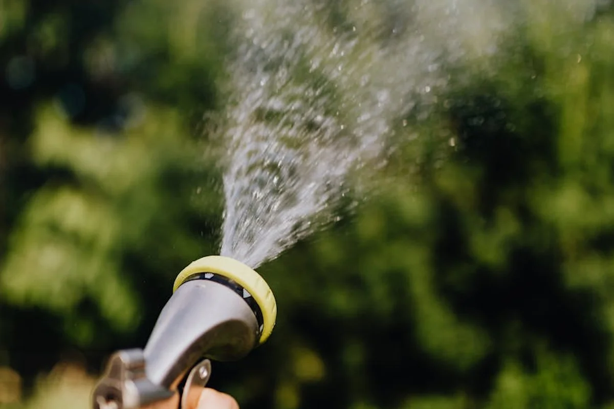 Sprinkler watering a lawn with a stream of water and a blurred green background