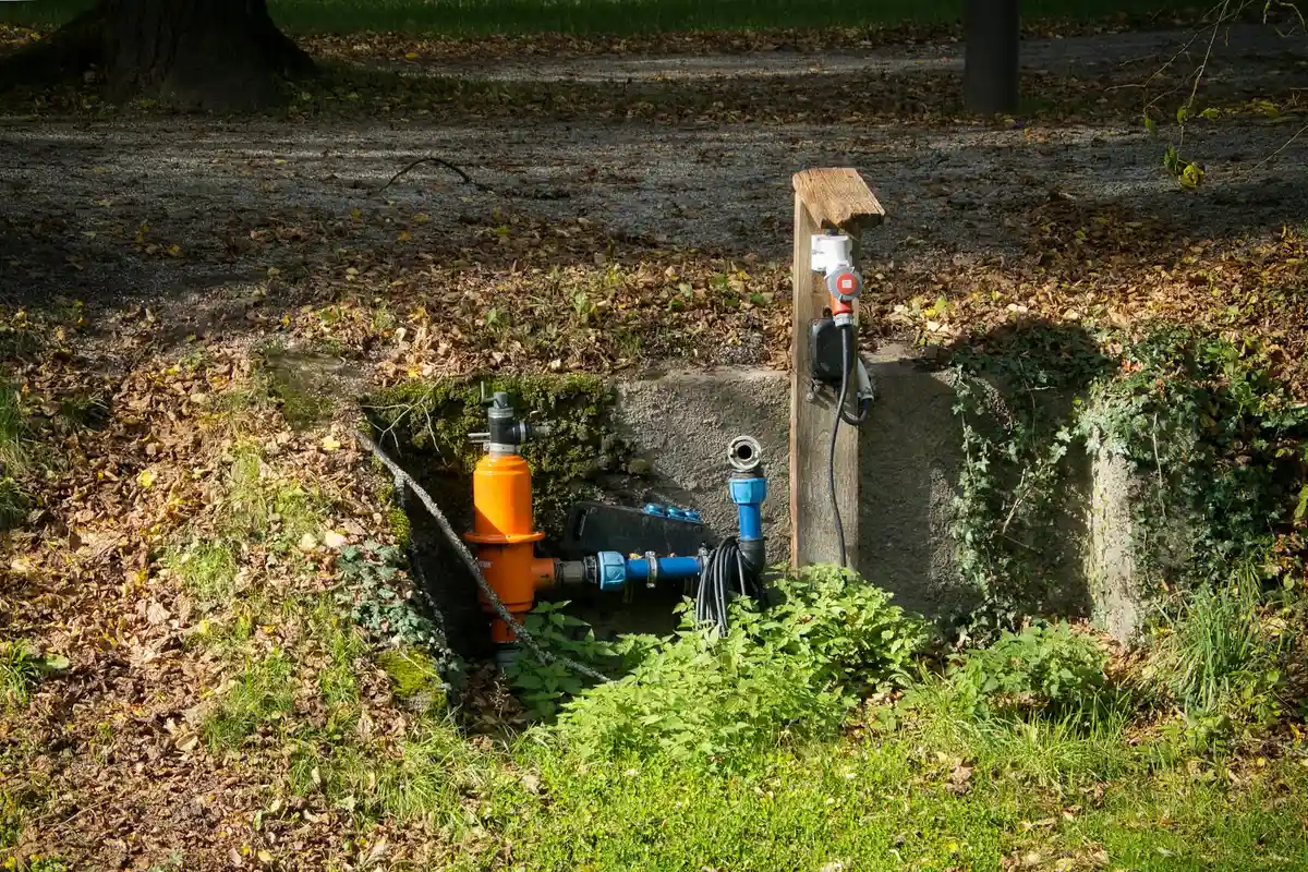 Underground sprinkler valve box with orange and blue valves and exposed piping during maintenance.
