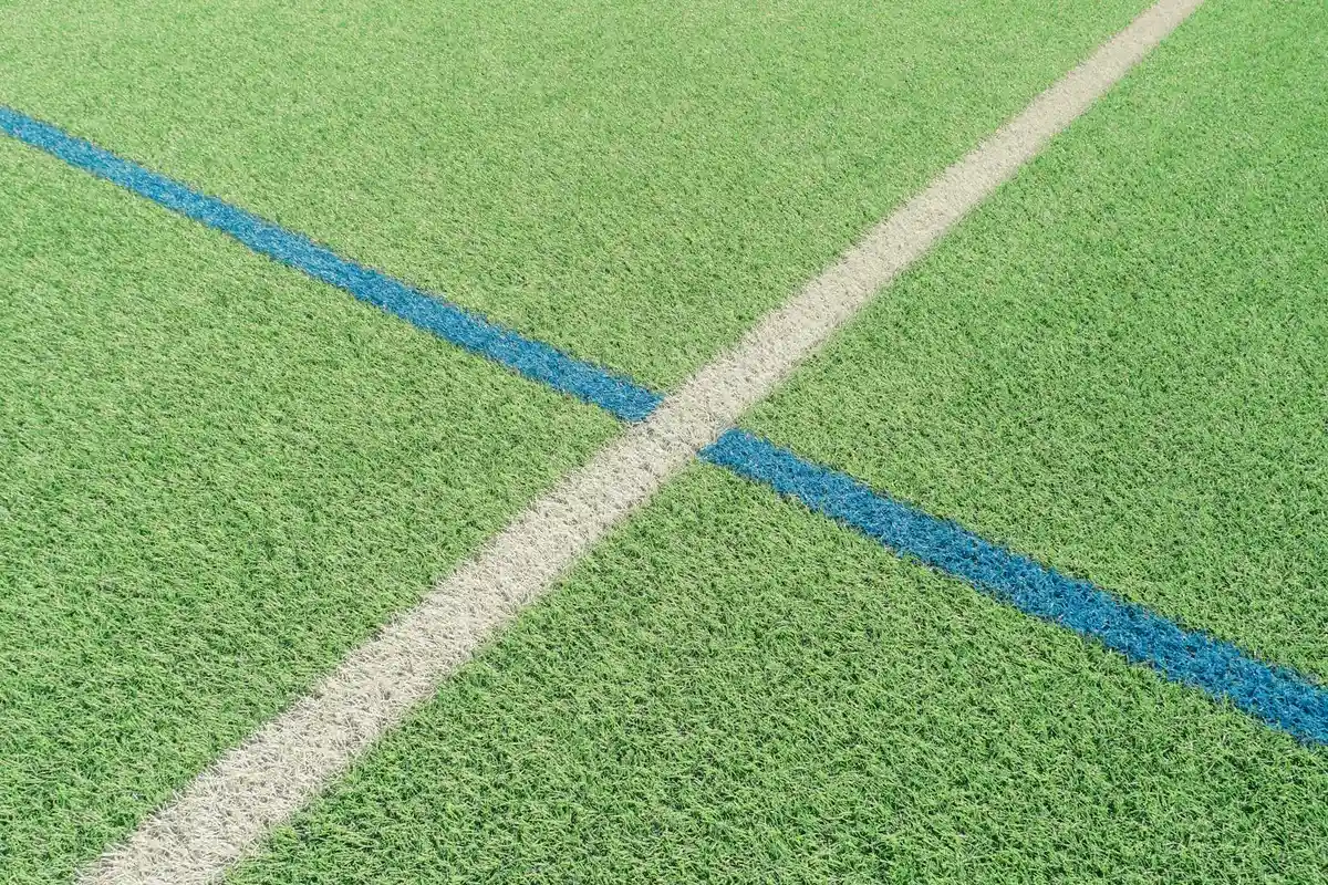Close-up of green turf with intersecting white and blue mowing lines forming crisp stripes