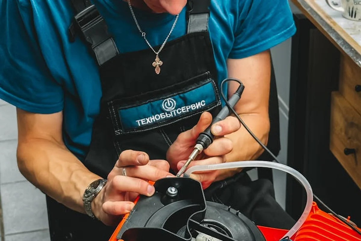Close-up of a person in a blue shirt and black apron using a tool on a red lawn mower, performing a simple repair