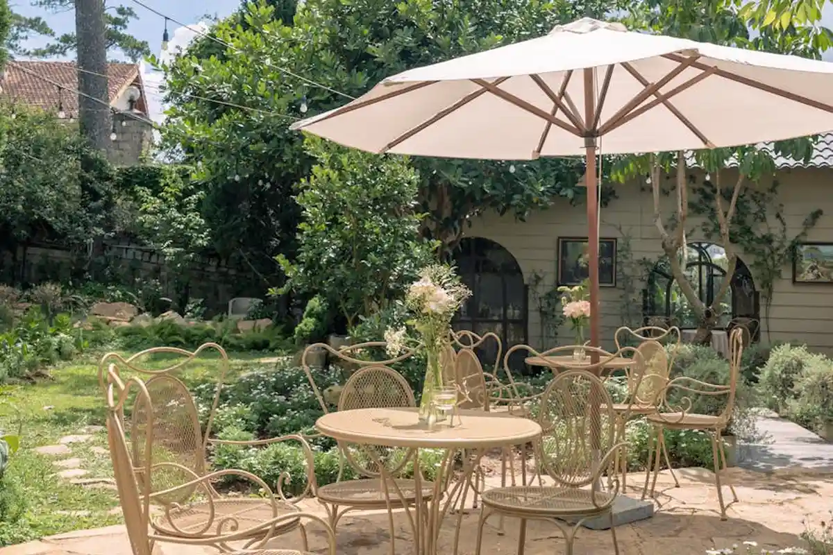 Cream-colored metal patio set with a round table and multiple chairs under a large white umbrella in a sunny backyard garden.