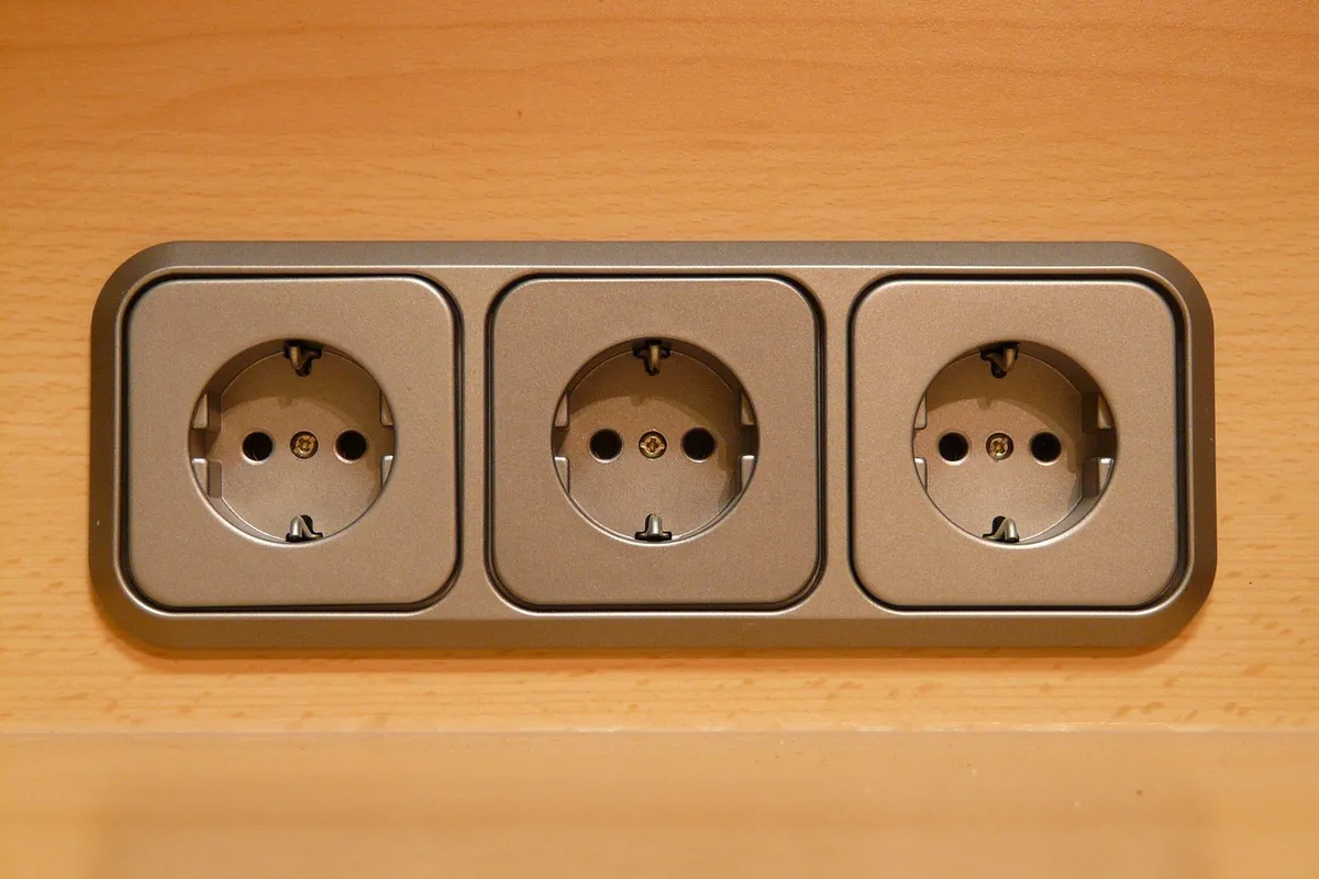 Three electrical outlets in a row mounted in a rectangular frame on a wooden surface